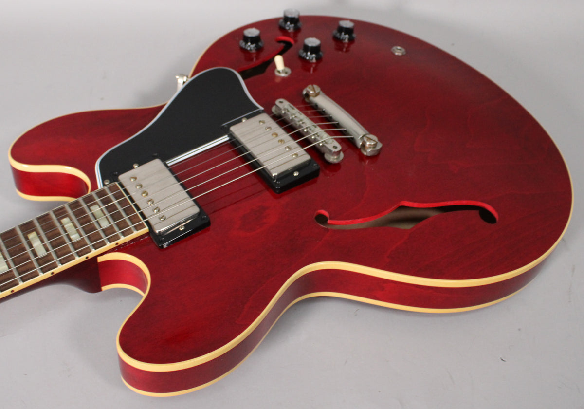 The cherry red semi-hollow guitar's body, f-hole, and lower neck are visible, showing light finish checking and binding.