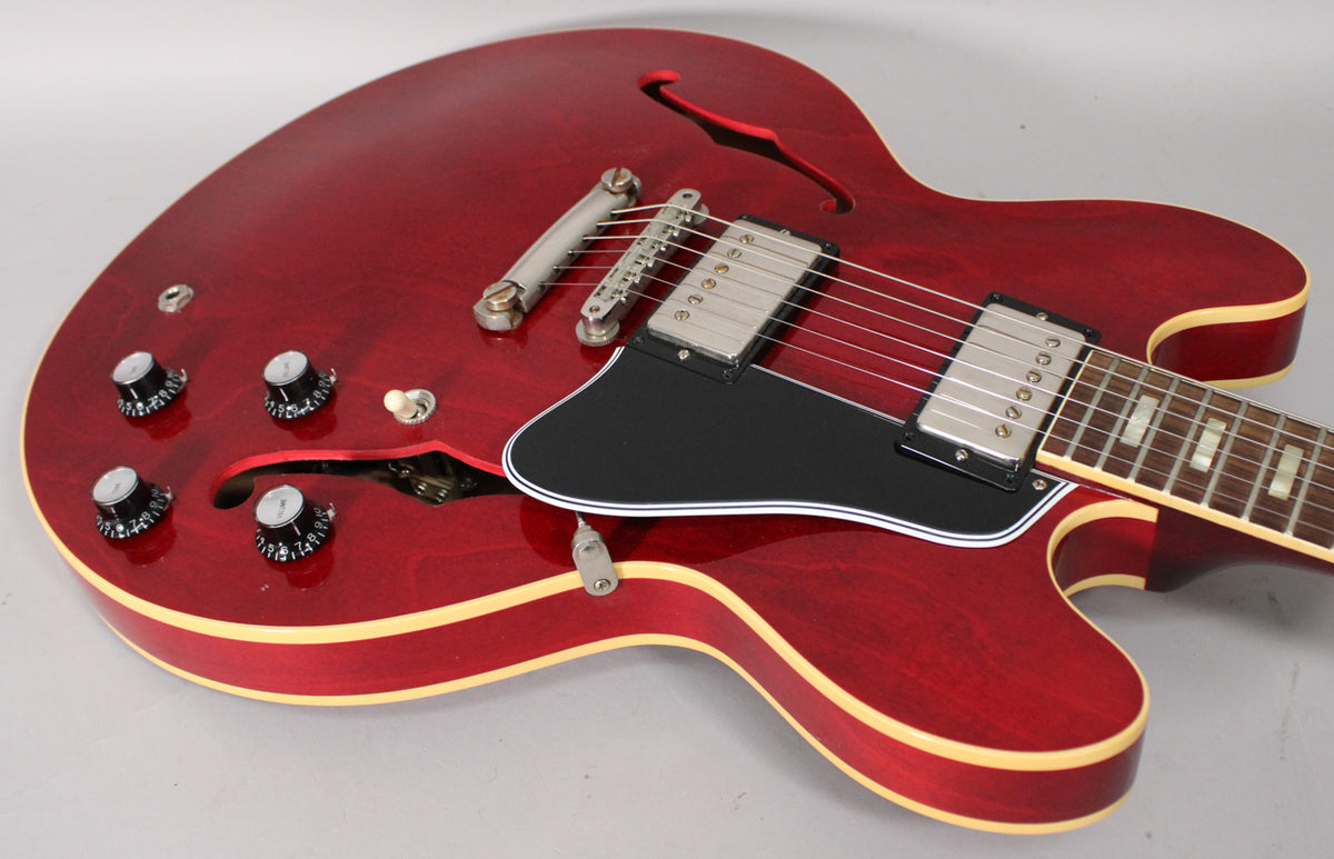 Upper body of a cherry red semi-hollow guitar with f-holes, black pickguard, four black knobs, and two humbucker pickups.