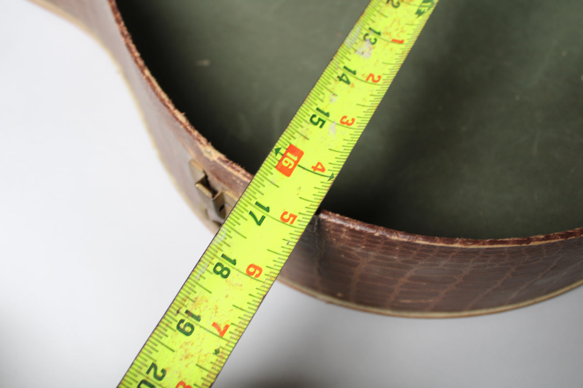 A yellow tape measure spans the open brown snakeskin case, revealing a dark green interior and a brass latch.