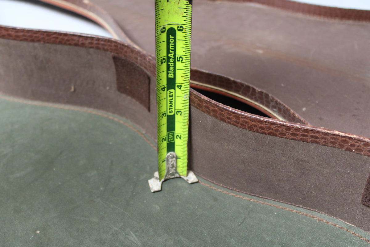 A tape measure shows the case's depth, with brown snakeskin-patterned trim on a worn green and brown exterior.