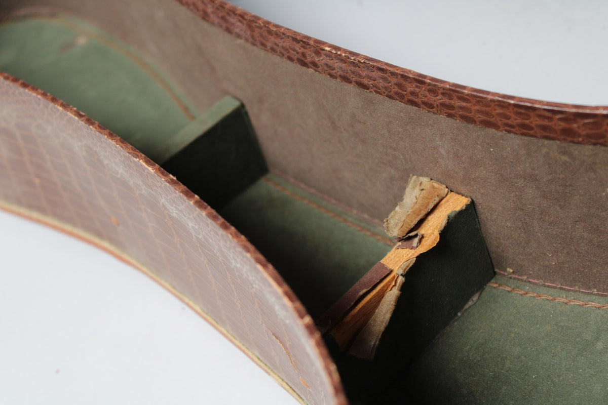 Close-up of the case interior, showing the brown snakeskin-patterned exterior, green lining, and a torn accessory compartment flap.