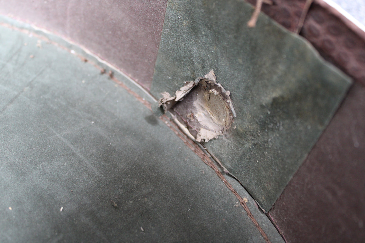 Close-up of the case's interior, showing a large hole in the green snakeskin lining and brown trim with visible wear and dust.