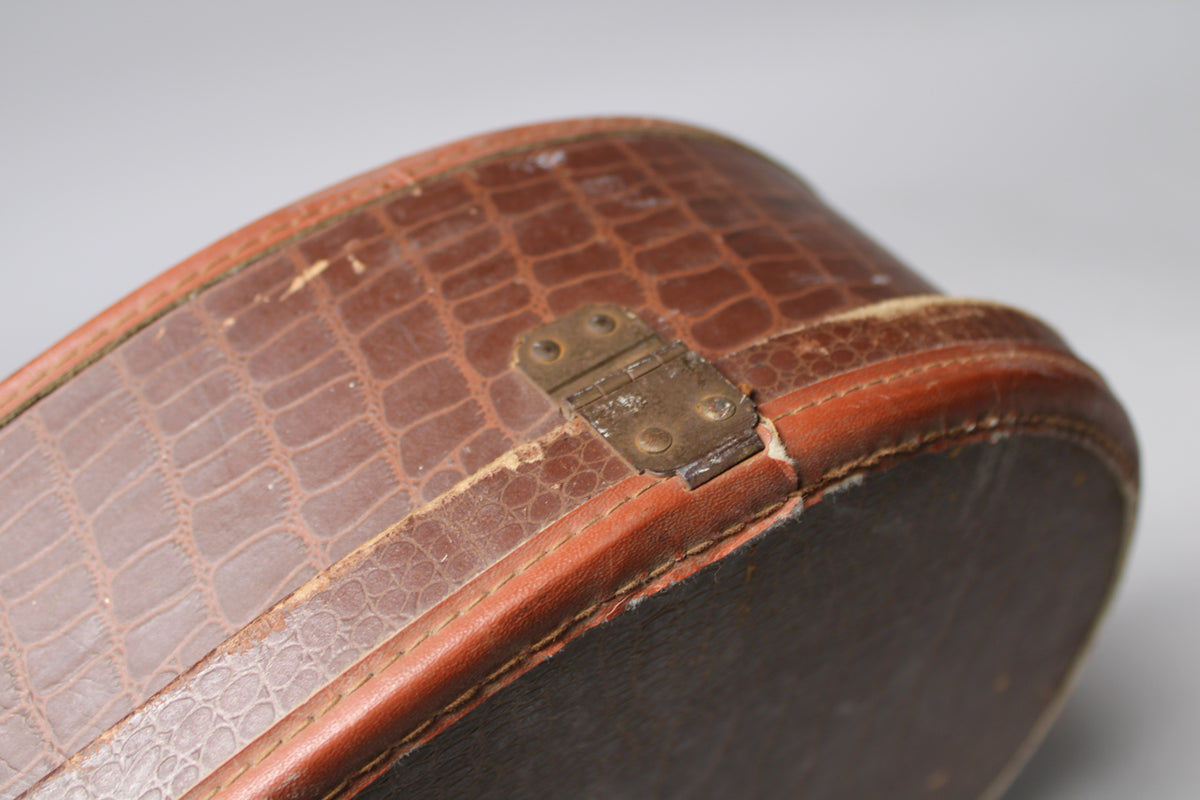 Close-up of a brown snakeskin-patterned guitar case, showing a tarnished brass hinge and worn edges with exposed material.