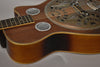 Close-up of the resonator guitar's body, showing its dark wood grain, two round chrome sound screens, and the tarnished metal resonator.