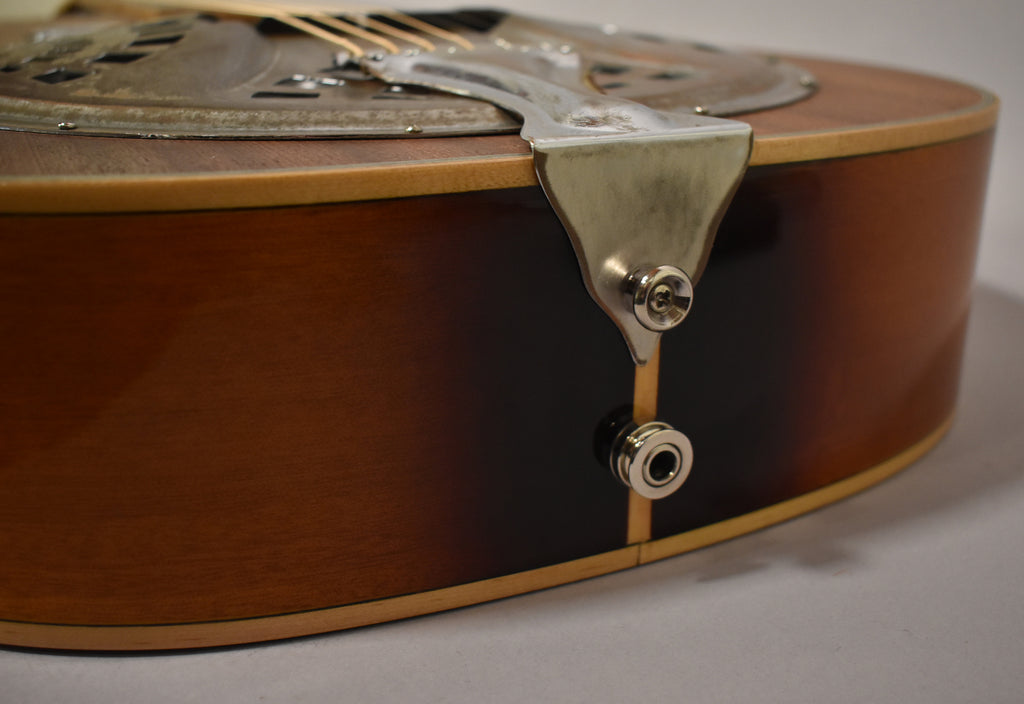 The resonator guitar's lower bout shows a dark brown sunburst finish, with a chrome strap button and input jack.