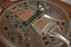 Close-up of the resonator guitar's distressed metal cover plate and tailpiece, showing rust-like patina and visible wear.