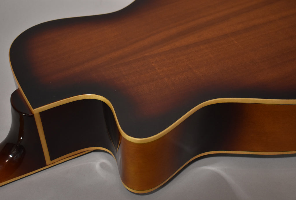 The resonator guitar's body, in a dark brown sunburst finish with light binding, is shown from the upper bout to the waist.