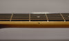 Close-up of the guitar's light brown neck and dark fretboard with copper strings, showing a single black dot inlay.