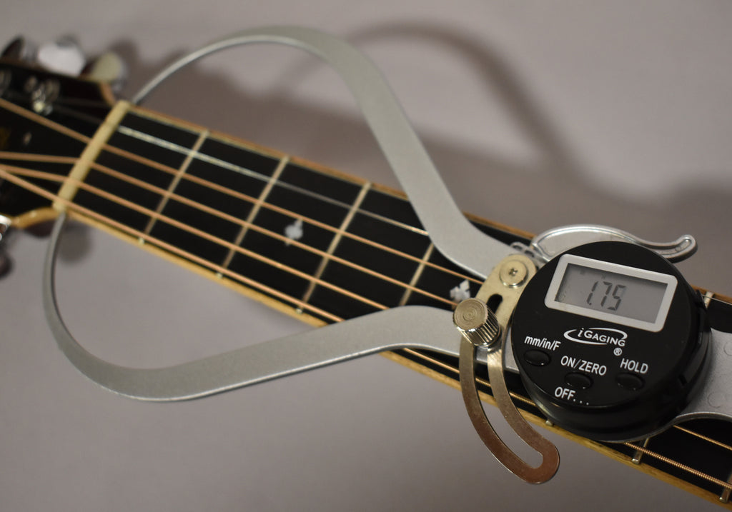 A digital caliper measures the nut width of the resonator guitar's dark fretboard, displaying "1.75" on its screen.