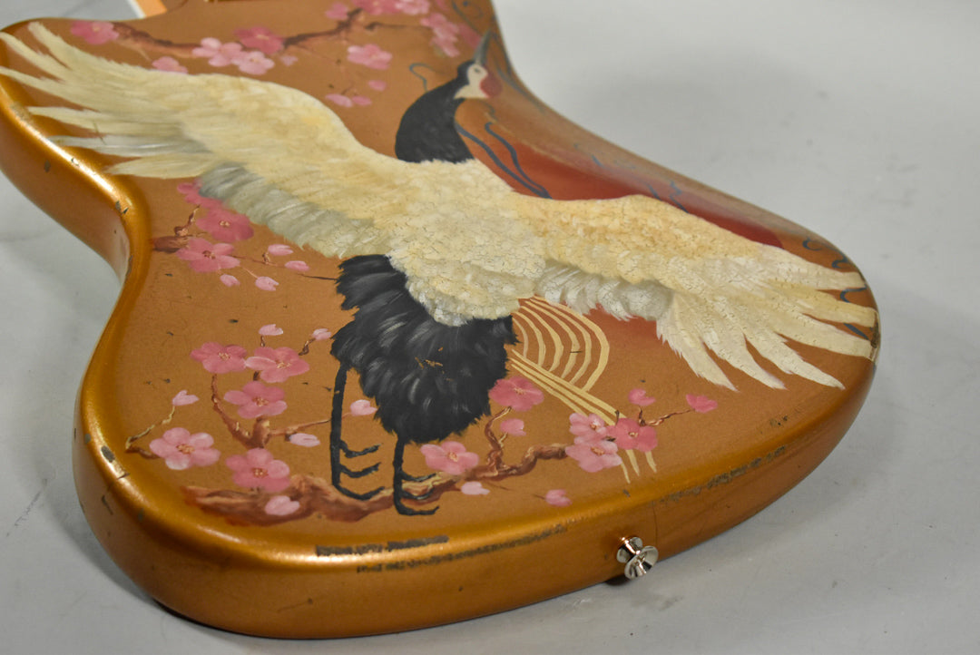 The guitar body's lower bout is painted with a large white crane and pink cherry blossoms on a metallic gold finish, with a chrome output jack.