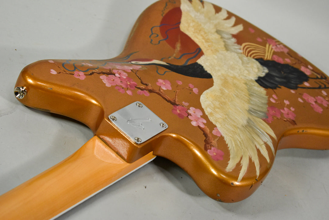 The guitar's metallic orange body, adorned with a hand-painted crane and cherry blossoms, shows minor wear near the input jack.
