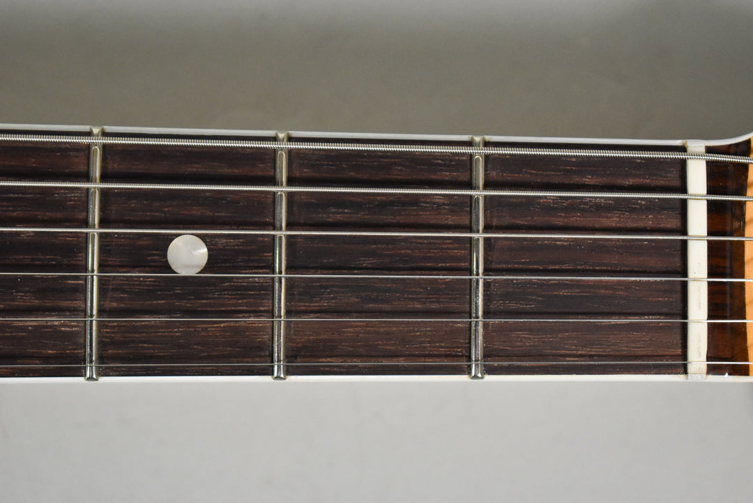 Close-up of the dark brown fretboard with silver frets and a single white circular inlay on the fifth fret.