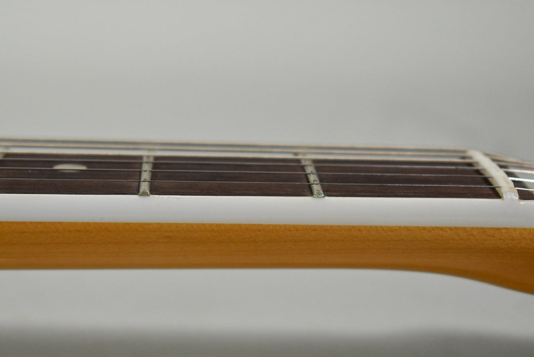 Close-up of the guitar's neck from the side, showing the light brown wood, white binding, dark fretboard, and metal frets.