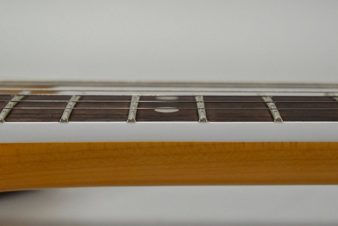 Close-up of the guitar's fretboard, showing dark wood, silver frets, and a single white dot inlay on the 7th fret.