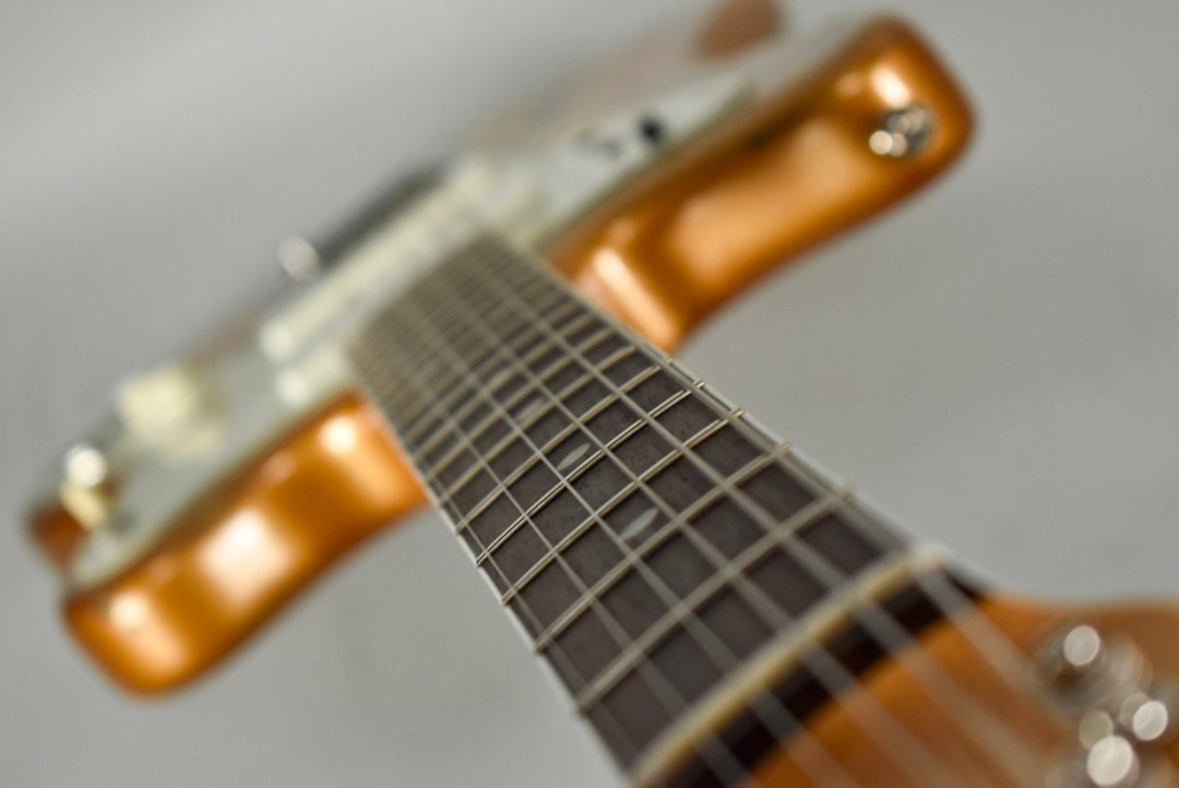 The guitar's dark fretboard and strings are in focus, angled from the headstock toward the blurred, metallic orange body.