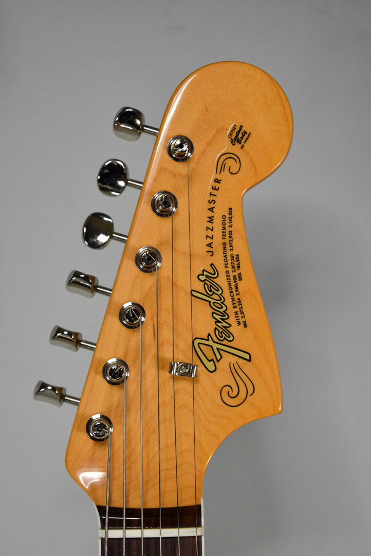 The Jazzmaster's maple headstock, angled left, features six chrome tuners, a string tree, and a dark brown fretboard.