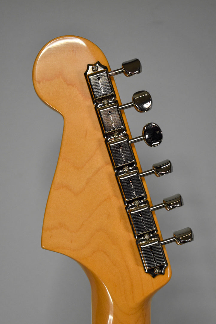 The back of a light maple headstock and neck, showing six chrome tuners with rectangular housings and oval buttons.
