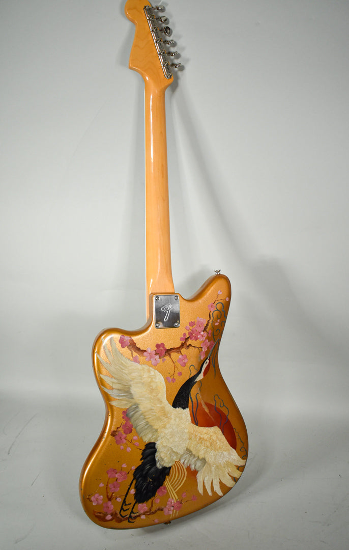 The back of a gold sparkle guitar with a large hand-painted crane and cherry blossoms, angled to show the neck and headstock.