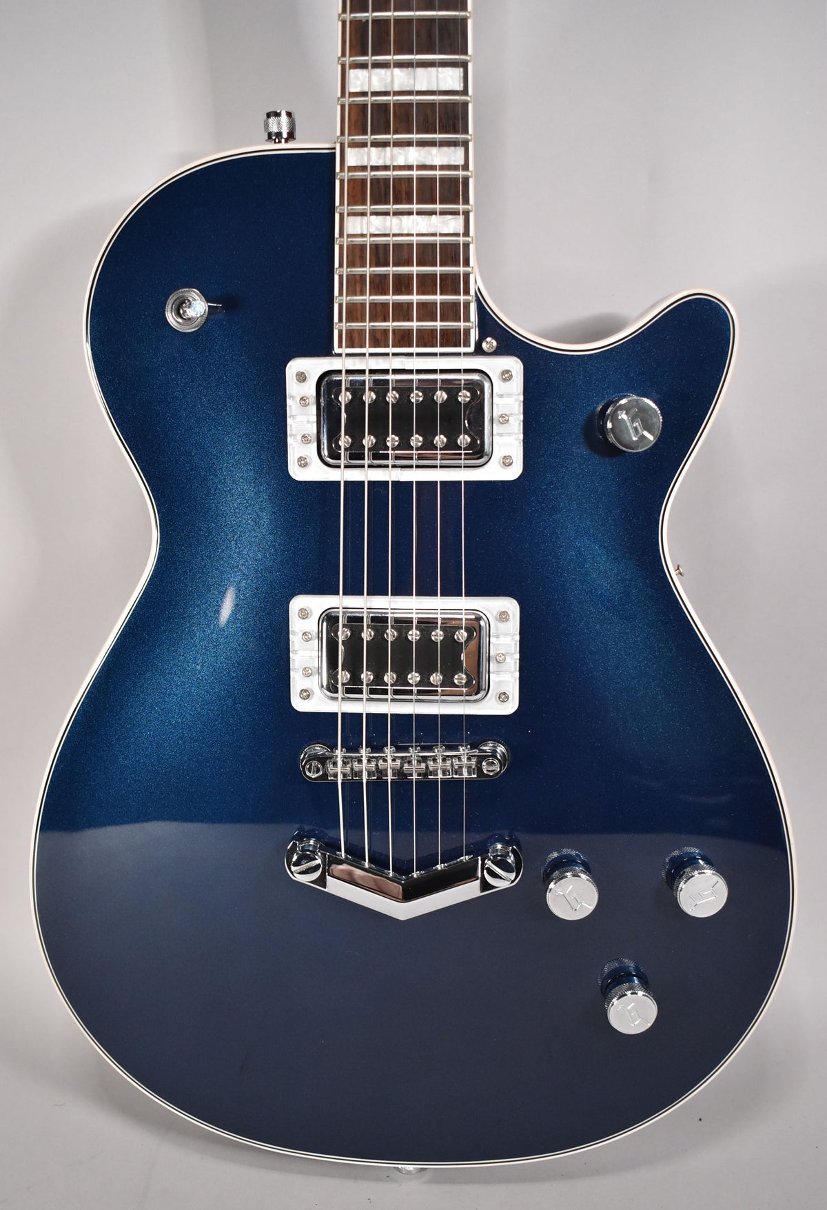 A full-frame, head-on view of a dark blue sparkle guitar body with cream binding, two humbuckers, and four chrome control knobs.