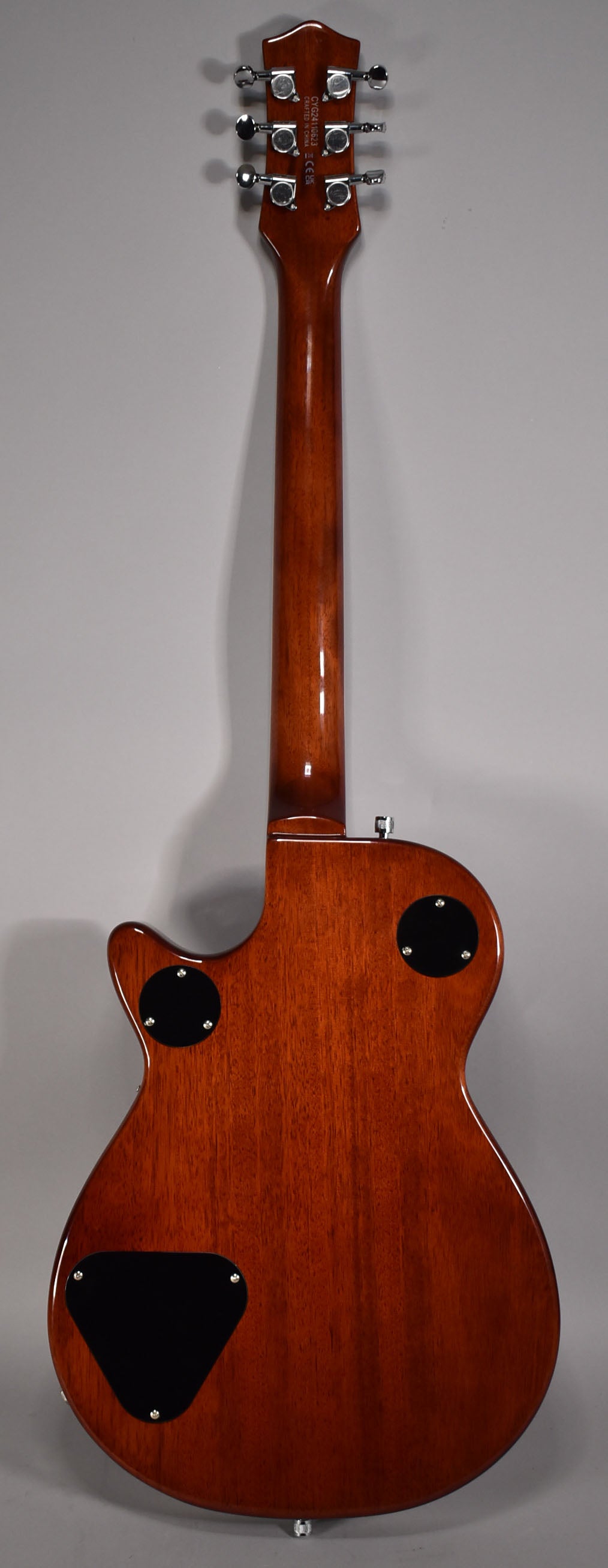 The guitar's back is a glossy reddish-brown, with three black control plates and six chrome tuners on the headstock.