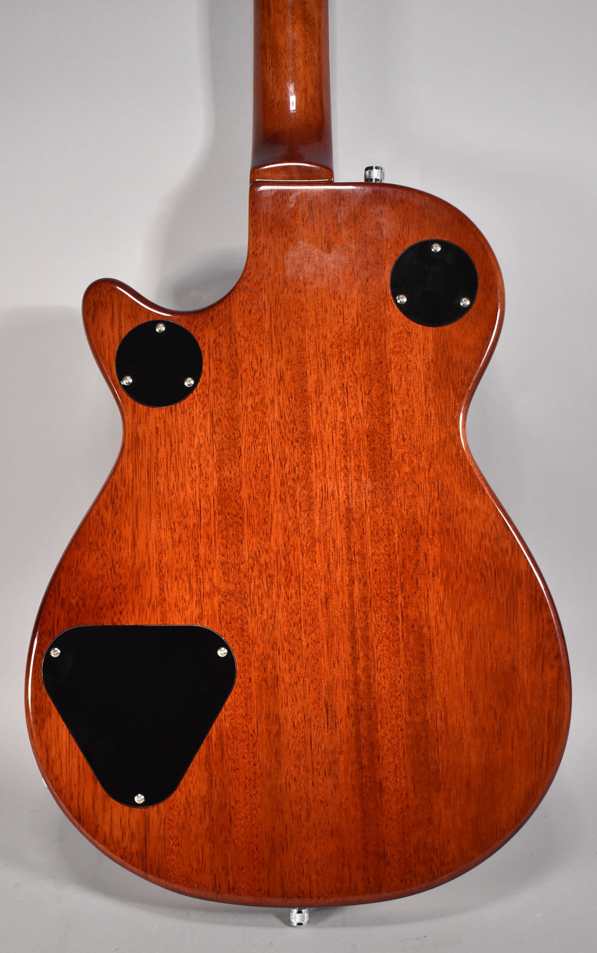 The guitar's back is a rich reddish-brown with visible wood grain, featuring three black control cavity covers and a chrome strap button.