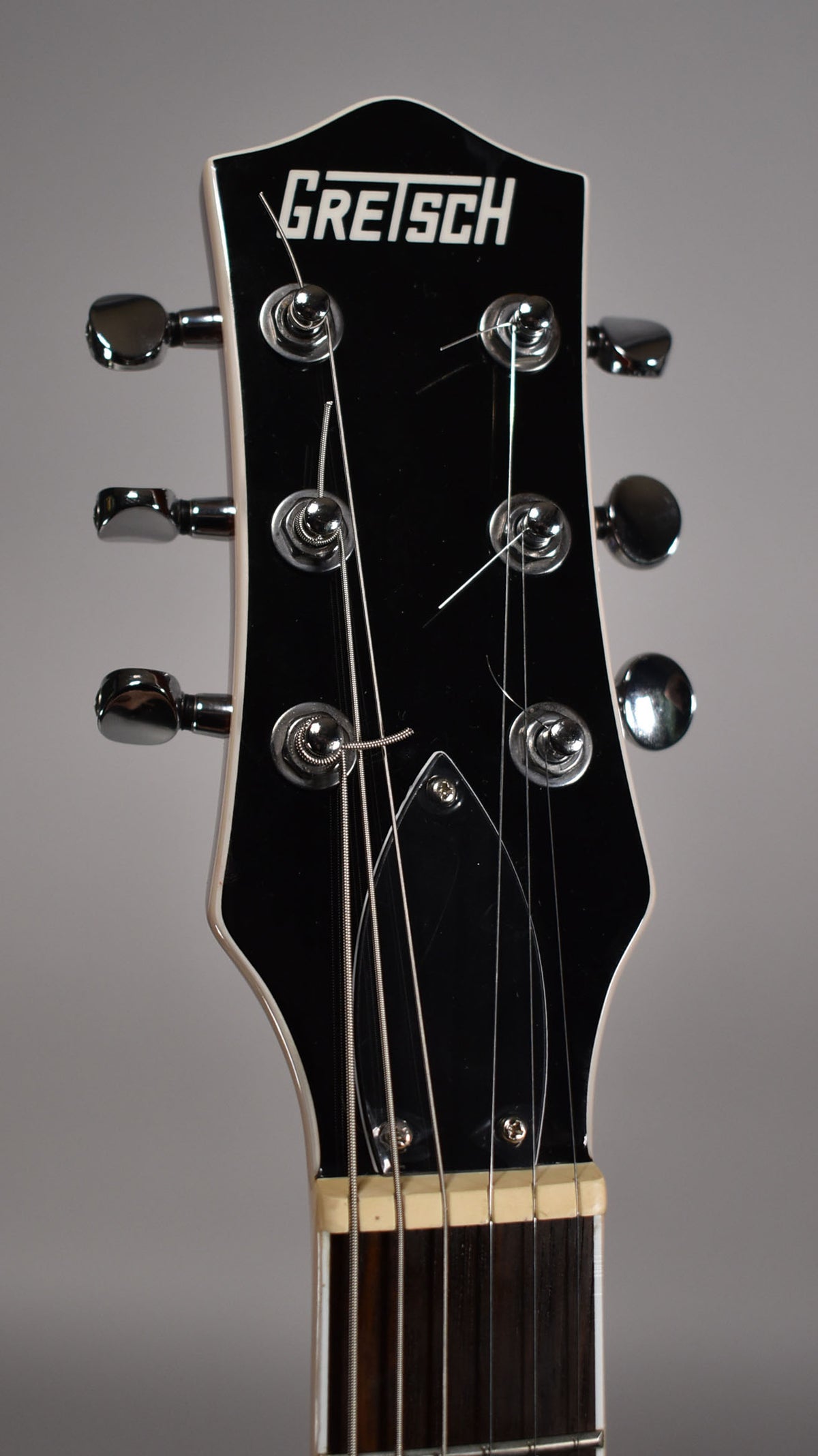 Close-up of the black headstock with white binding, showing six chrome tuners, a string tree, and the nut.