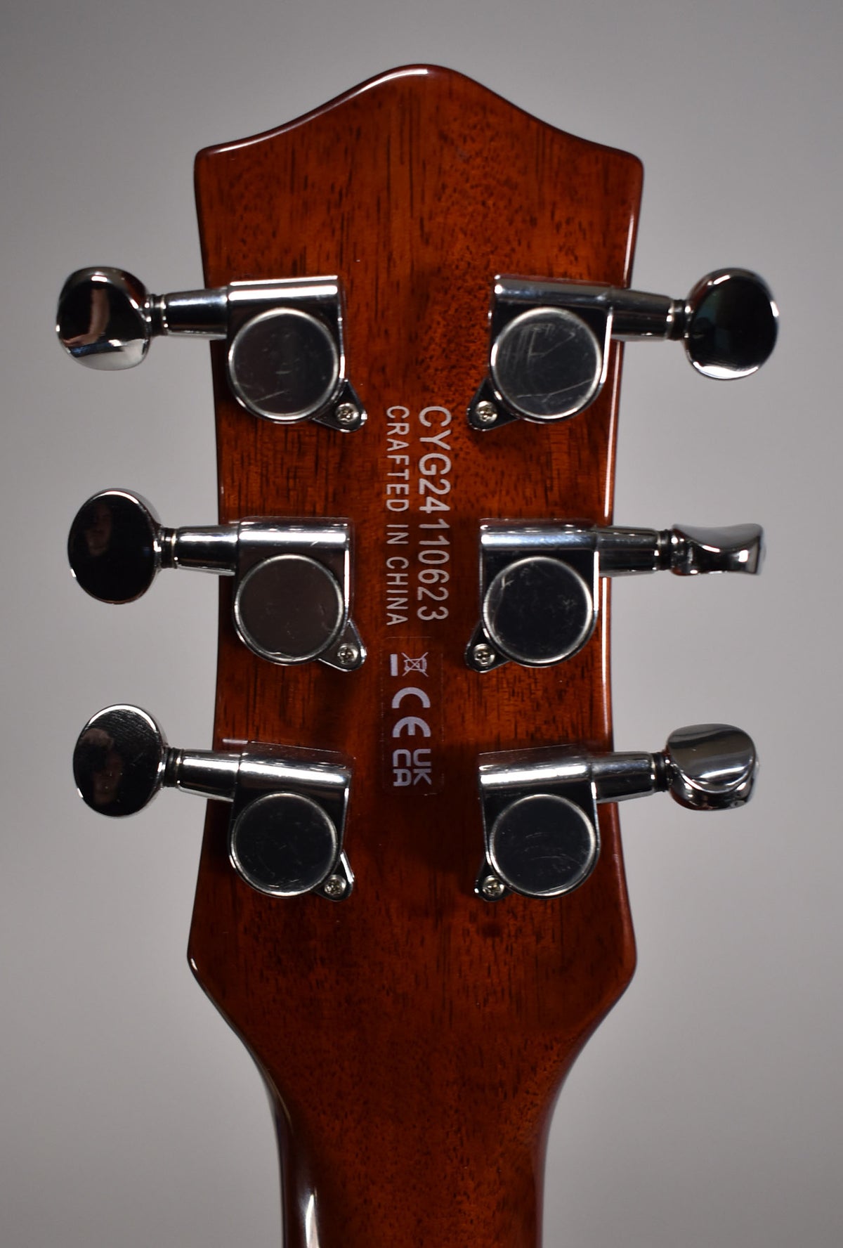The back of the guitar's headstock, showing a glossy dark brown finish and six chrome tuning machines with light scuffs.
