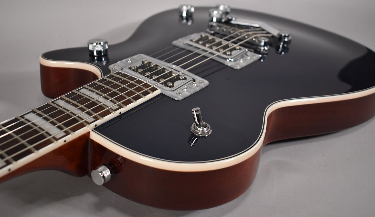 The dark grey guitar body, with cream binding and brown sides, is angled to show the neck, two chrome humbuckers, and a toggle switch.