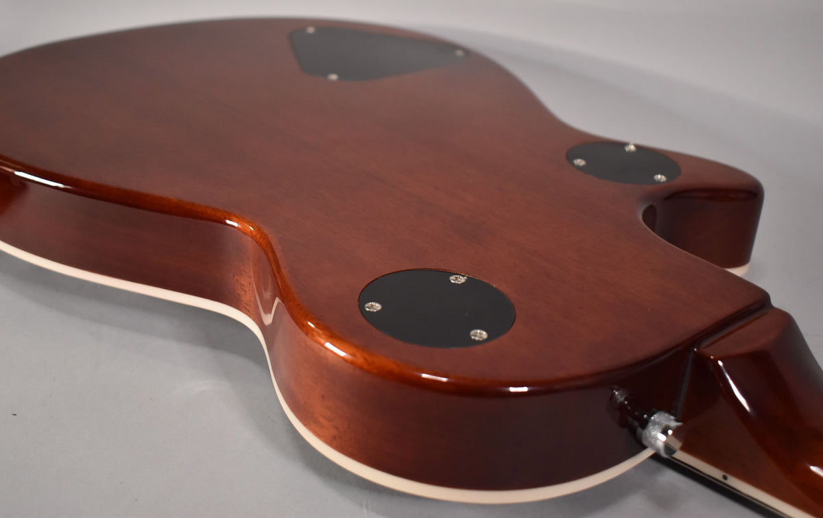 The guitar's back, a glossy dark brown with visible wood grain, shows two black control plates and a chrome output jack.