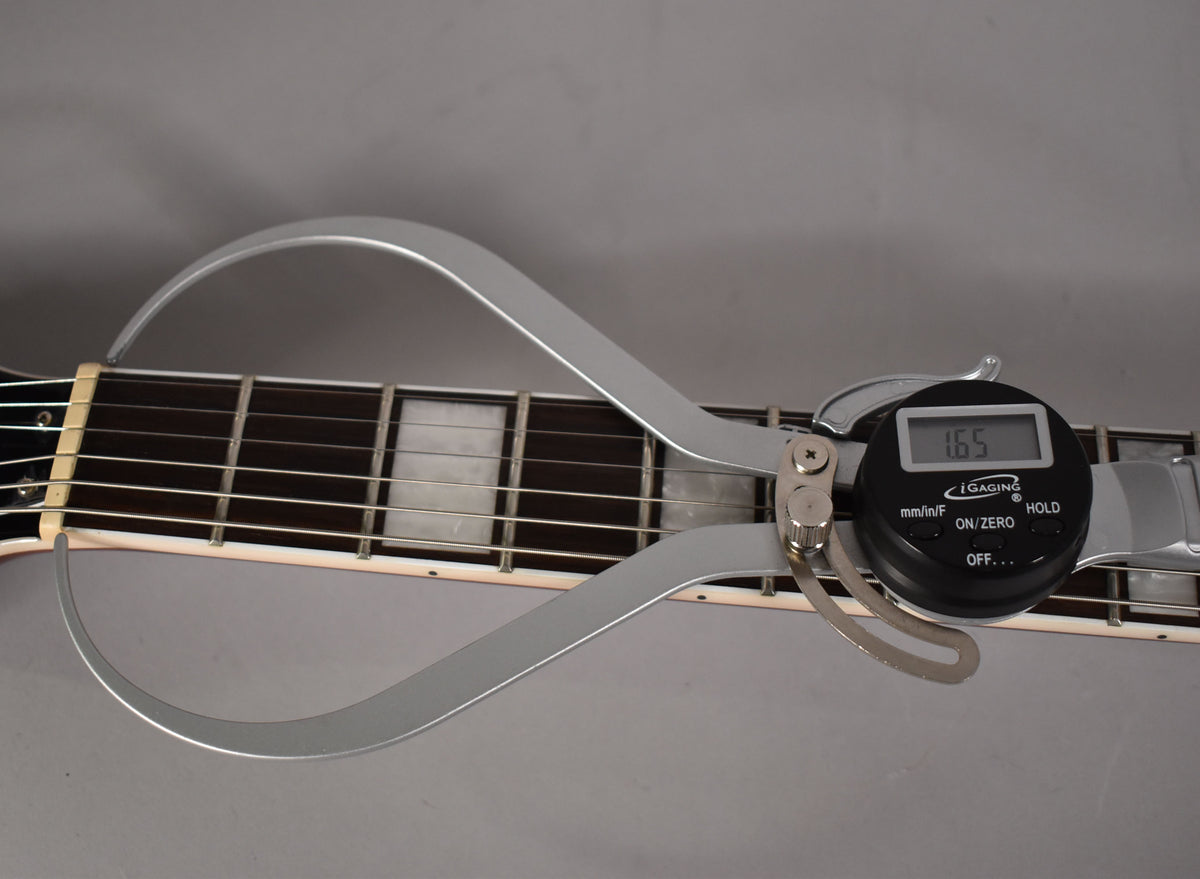 A digital caliper measures the guitar's nut width at 1.65 inches, with block inlays visible on the dark fretboard.