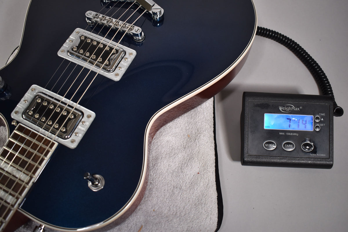 Close-up of the guitar's metallic blue body and chrome hardware, with a digital scale displaying "7.74" to the right.