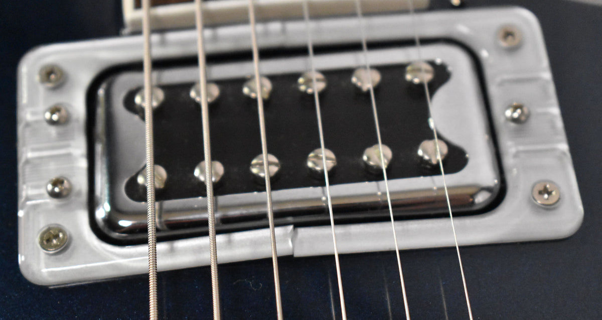 Close-up of the bridge pickup, showing a chrome humbucker with visible pole pieces, mounted in a clear plastic surround.