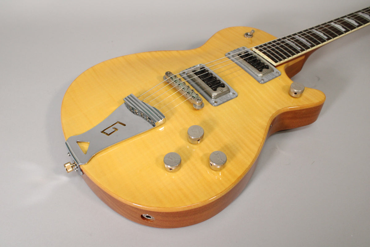 Antique maple electric guitar, angled from the lower bout, showing the Bigsby-style tailpiece, two humbuckers, and three chrome knobs.