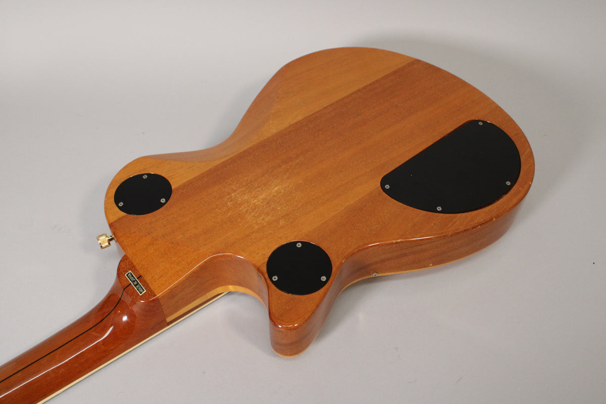 The guitar's antique maple body, viewed from the back, shows three black control cavity covers and light wear on the finish.