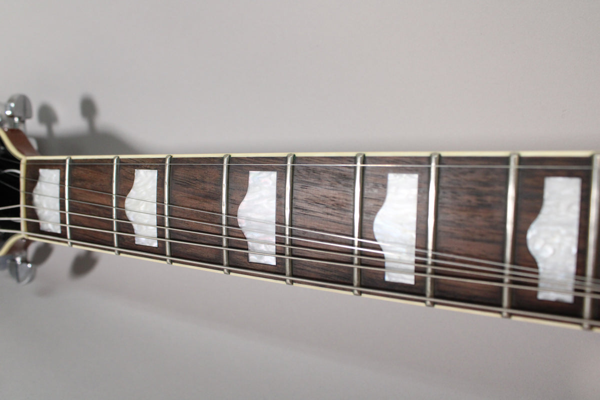 Close-up of the dark wood fretboard with white pearloid block inlays, showing the frets and strings from a slight angle.