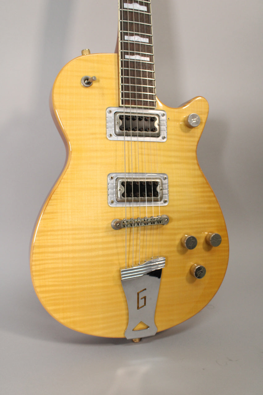 The antique maple electric guitar is angled, showing its flame top, two humbuckers, four chrome knobs, and a "G" logo tailpiece.