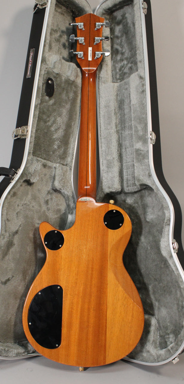 The back of the guitar, in antique maple with a glossy finish, rests in a plush-lined hard case, showing the headstock and tuning pegs.