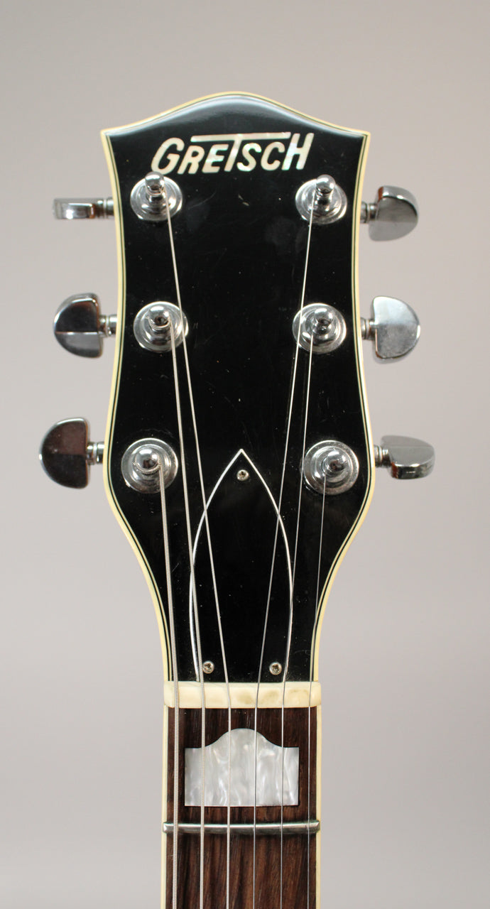 Close-up of the guitar's black headstock with white binding, chrome tuners, and a mother-of-pearl inlay on the dark fretboard.
