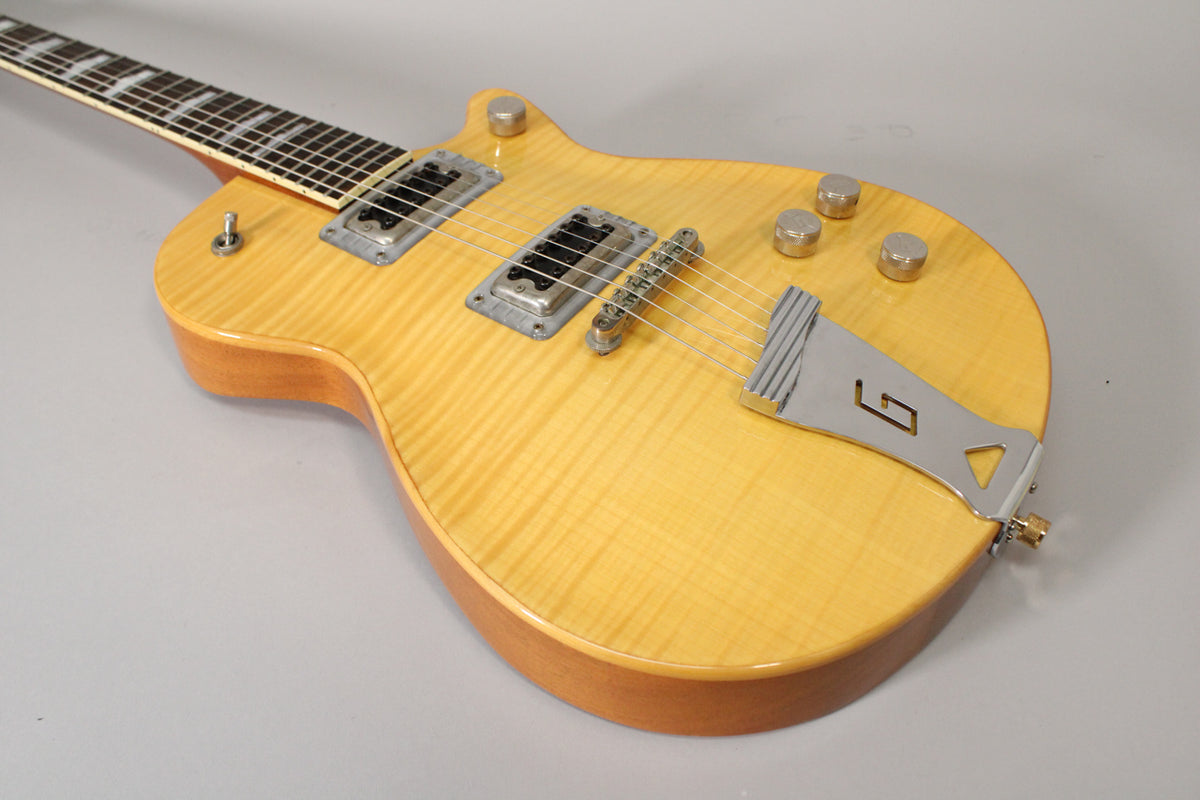 The antique maple guitar body, with a visible flame top and natural sides, is angled to show the neck, two humbuckers, and a G-cutout tailpiece.
