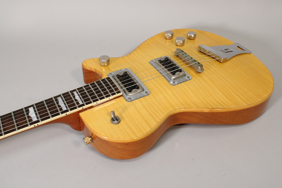 The antique maple guitar body, with a flamed top and natural sides, features two humbuckers, four knobs, and a toggle switch.