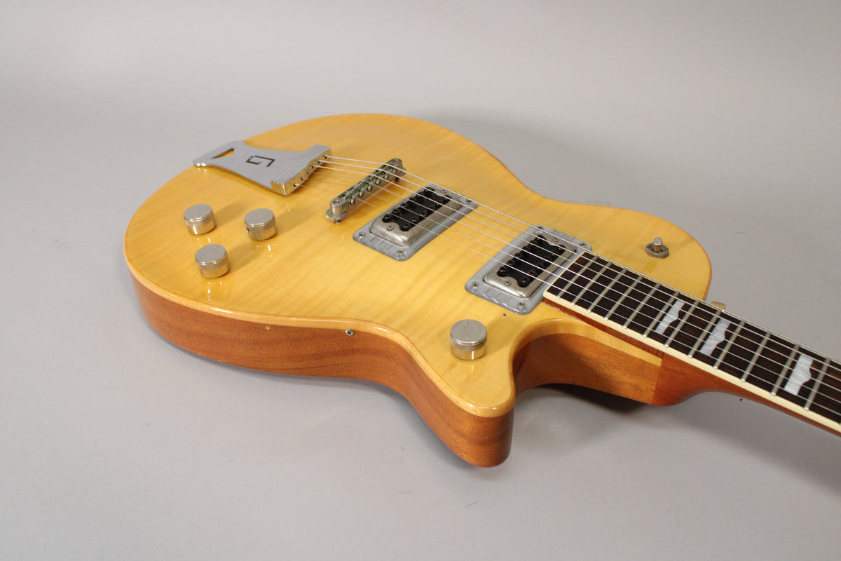 The antique maple guitar body, with a visible wood grain, features four chrome knobs, two humbuckers, and a chrome tailpiece.