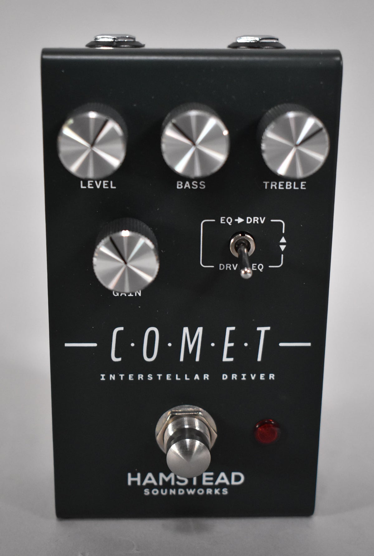 A black guitar pedal with four silver rotary knobs, a small toggle switch, a large footswitch, and a red LED.