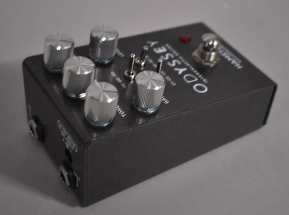 Dark grey pedal with five silver knurled knobs, three small toggle switches, a red LED, and a silver footswitch.