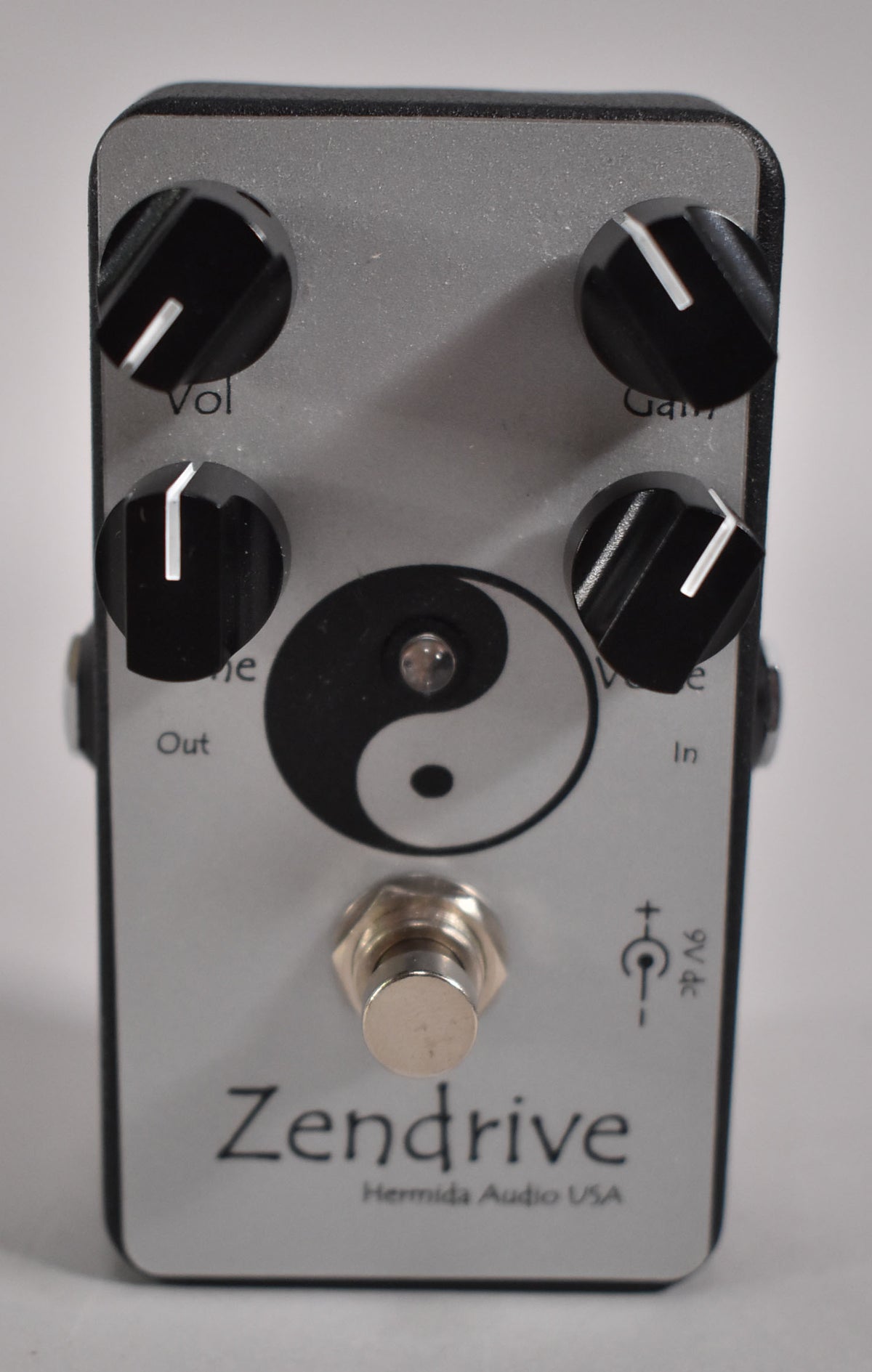 A silver guitar pedal with a black frame, four black control knobs, a yin-yang symbol, and a chrome footswitch.