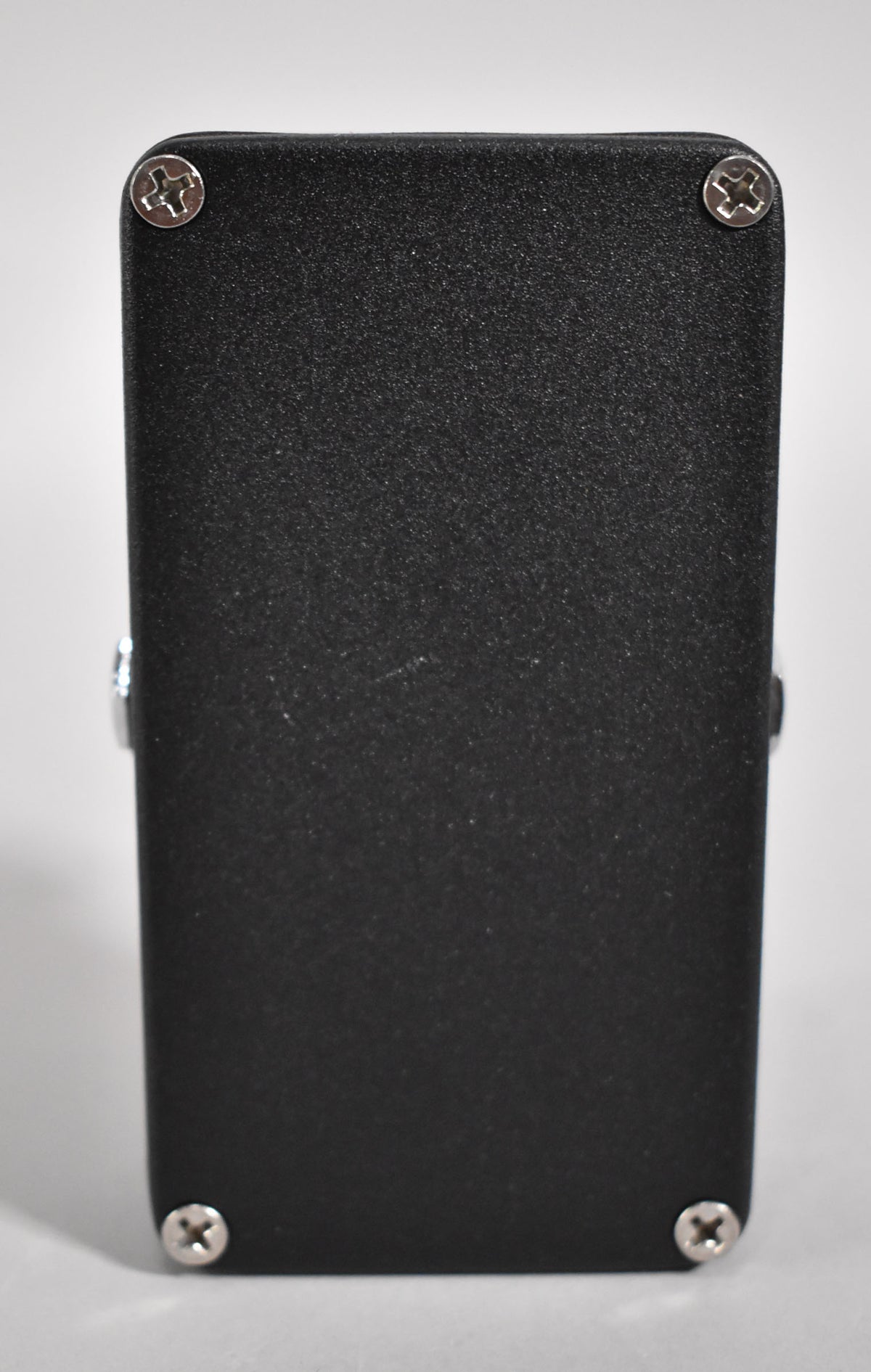 The pedal's textured black metal casing is viewed from the back, showing four silver Phillips head screws and light surface scuffs.