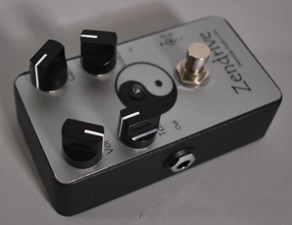A silver-faced guitar pedal with a black base, four black control knobs, a silver footswitch, and a yin-yang symbol.