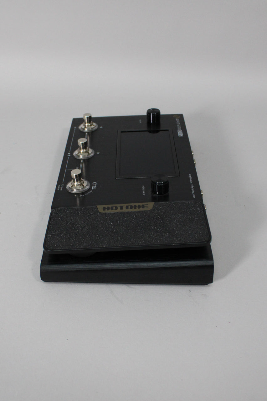 A black multi-effects pedal with three silver footswitches, a black expression pedal, a screen, and two black control knobs.
