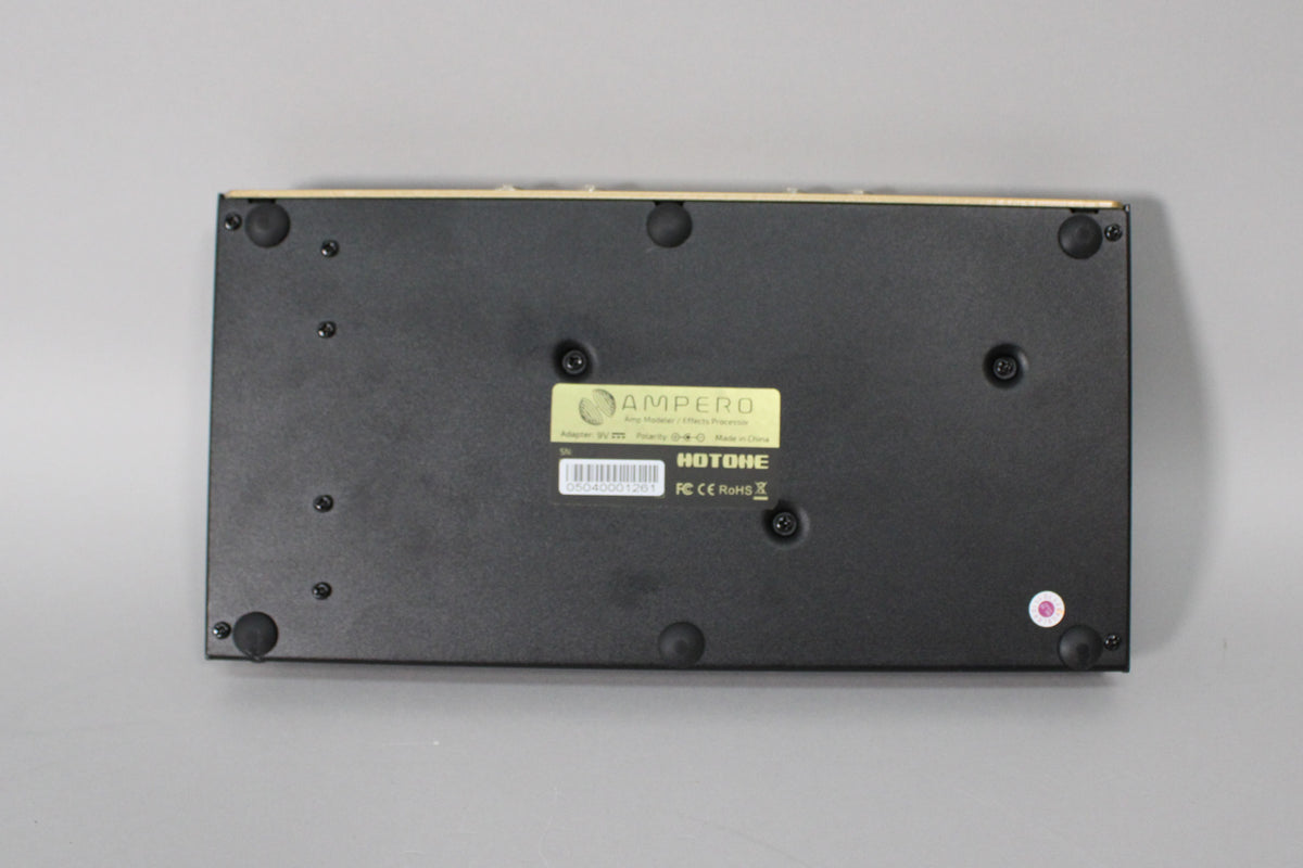 The black metal bottom of the pedal is shown, with eight visible screws, four rubber feet, and a yellow product label.