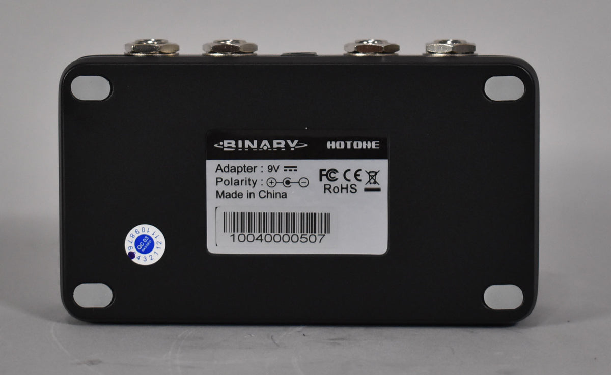 The black pedal's underside is visible, showing a white label with text and a barcode, plus four silver feet and a blue QC sticker.