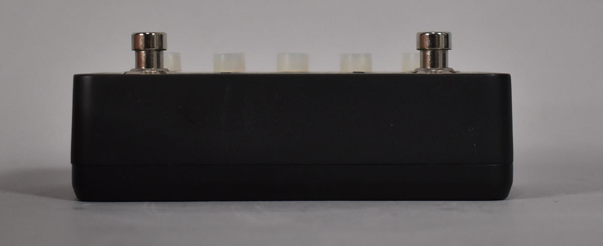 The black pedal is viewed from the front, showing two chrome footswitches and three translucent knobs on top.
